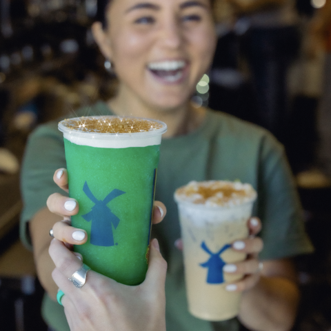 A smiling broista handing two drinks out the window.